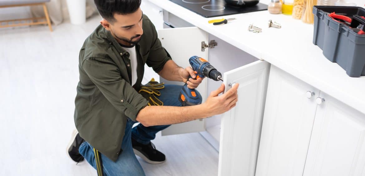 man wearing a green shirt renovating the kitchen cabinets in a home.