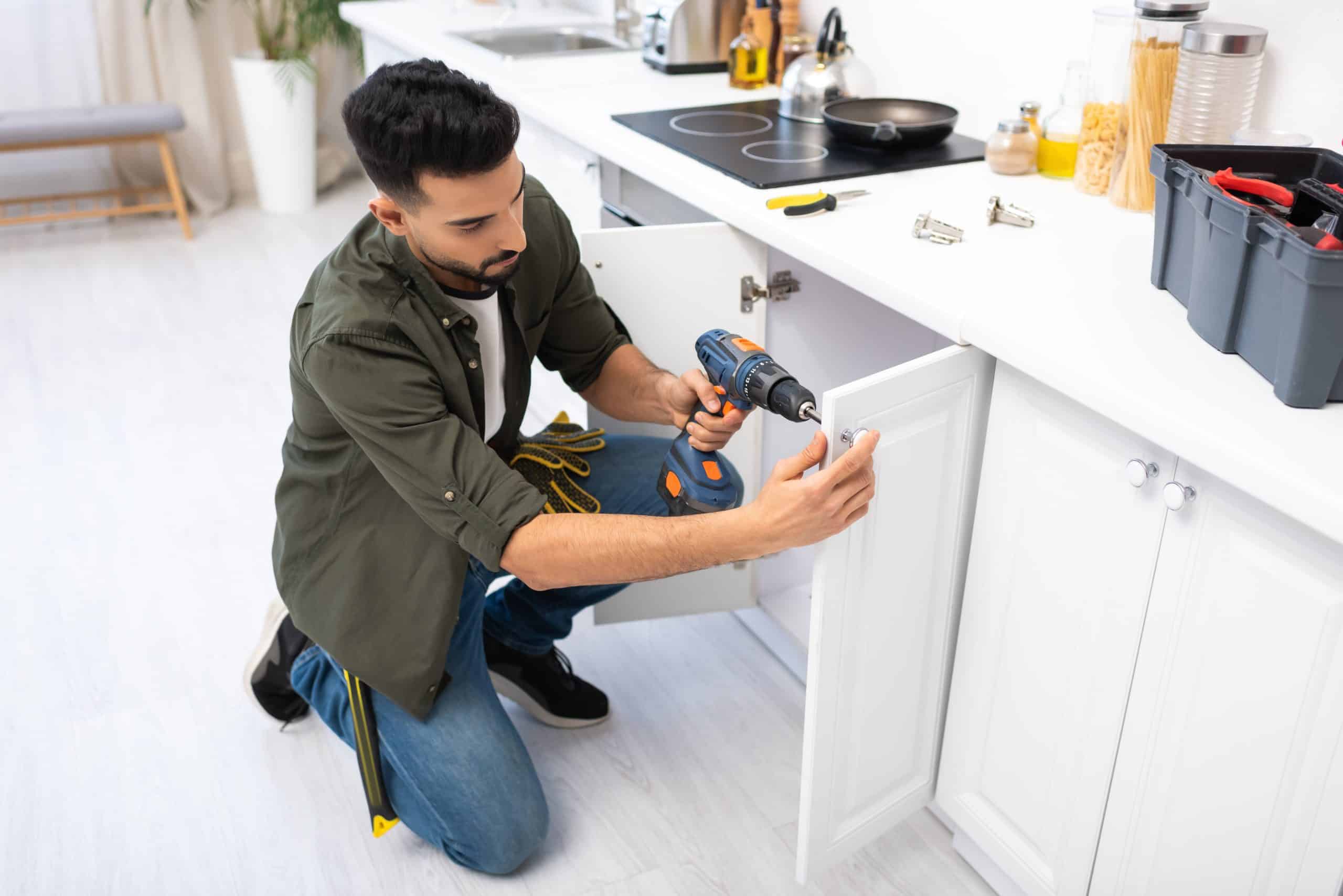 man wearing a green shirt renovating the kitchen cabinets in a home.